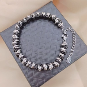 Detail of black and white stainless steel chain bracelet with S-STEEL tag on display pad