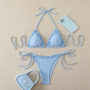 Detail of light blue striped bikini set with ruffled edges on a beige beach texture