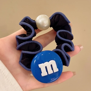 Détail d'un chouchou en tissu avec perle et pendentif bleu orné de la lettre 'm' blanche