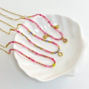 Detail shot of pink natural stone beaded necklaces with 18K gold plated charms on a shell dish
