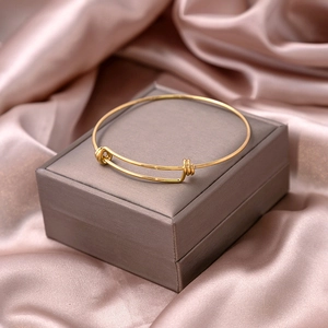 Detailed view of a gold-plated adjustable knot bangle resting on elegant champagne silk