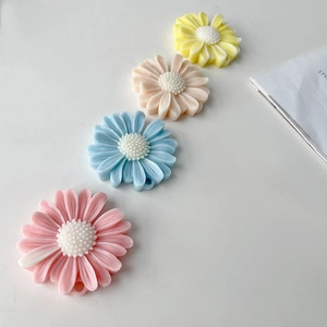 Detailed view of four colorful daisy resin accessories in pink, blue, beige, and yellow