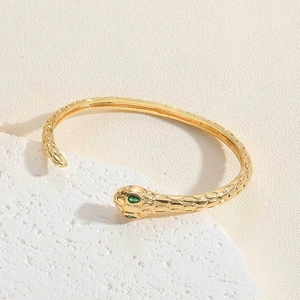 Macro detail of golden snake bracelet with green gem eyes and textured scales on stone