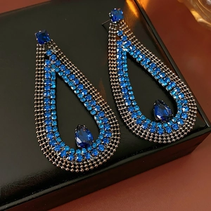 Macro shot of blue teardrop earrings with crystals on a textured black leather surface