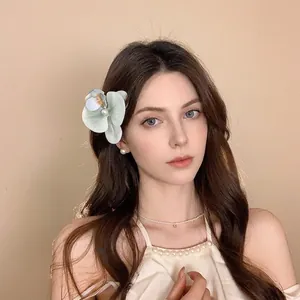 Elegant floral hair clip with gradient petals and pearls worn by a model in soft lighting