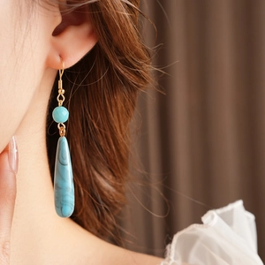 Dettaglio di orecchini boho con gocce di marmo blu e ganci dorati indossati da modella