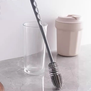 Close-up of the grey silicone brush head and long handle inside a clear glass cup