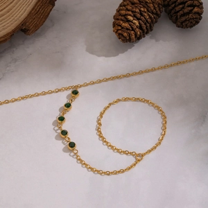 Close-up of gold chain featuring five green zircon stones on stone background