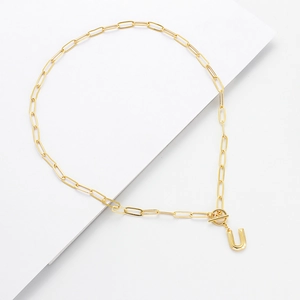 Detail of golden paperclip chain necklace with toggle clasp and letter U pendant