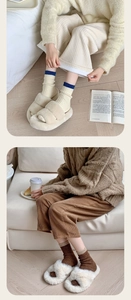 Detailed view of thick wool socks paired with plush slippers and corduroy trousers