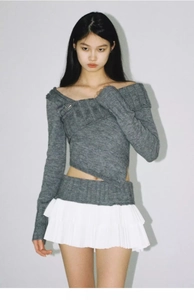 Detail showing asymmetric knit top hem with layered white pleated mini skirt texture