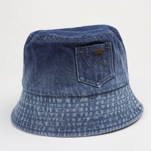 Gros plan du chapeau bob en jean délavé avec poche latérale et emblème métallique vintage