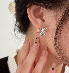 Close-up of elegant silver bow-shaped earring on ear showing delicate hollow design