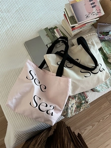 Detail of pink and white canvas tote bags with See Sea print on a textured bed sheet