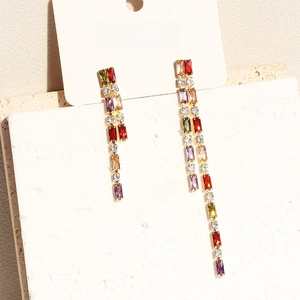 Asymmetric gold tassel earrings with colorful zircons on stone display stands