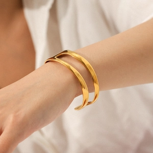 Asymmetric open cuff bangle in 18K gold plated titanium steel worn by a fashion model
