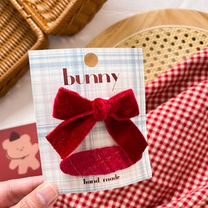 Detailed view of a handmade red velvet bow hair clip on a grid card held in hand