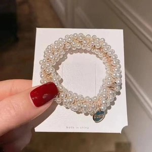 Detail of cream pearl elastic hair ring featuring a gold love charm on a display card
