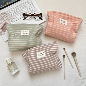 Three striped canvas makeup bags with zip closure and woven brand labels on white background