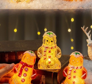 Close-up of glowing gingerbread man and snowman LED Christmas ornaments on snowy surface