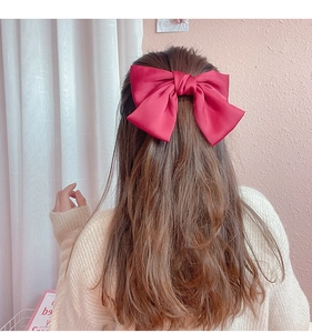 Detail of a large red satin bow hair clip on brown hair with elegant silky texture