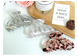 Three acetate hair claws in marble, pearl, and tortoiseshell finish on a wooden tray