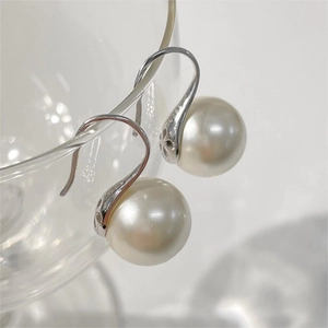 Macro shot of S925 sterling silver pearl earrings hanging on a clear glass edge