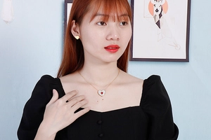 Close-up of model wearing gold heart necklace with red gem and matching stud earrings