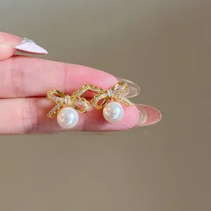 Detail of 18K gold plated bow earrings with sparkling zircon and large white pearls