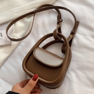 Mini sac à bandoulière en cuir marron avec poignée en U sur fond de tissu blanc doux