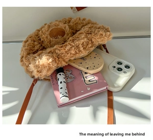 Close-up of brown plush bear crossbody bag with zipper and woven strap on white desk