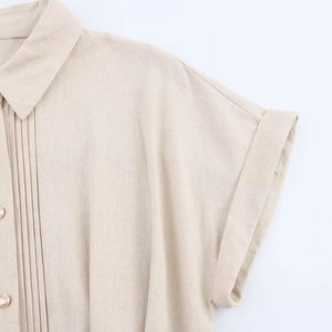 Detail of beige cotton linen shirt with pleated V-neckline and gold decorative buttons