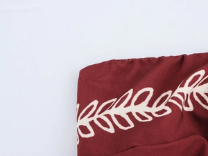 Detail view of ethnic print on deep red fabric with white leaf patterns and stitching
