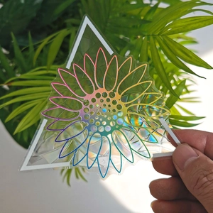 Holographic sunflower prism window sticker held by hand against green plants