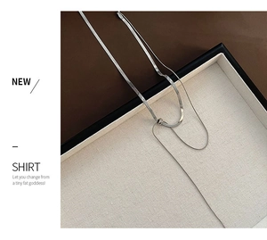 Detail view of double-layered silver snake chain necklace on white fabric texture tray
