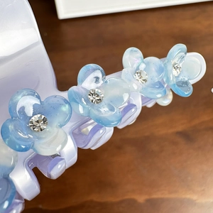 Lavender acetate hair claw clip with blue rhinestone flowers on a wooden background