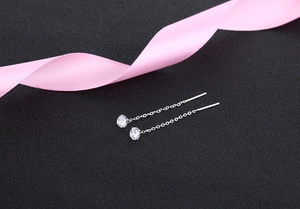 Macro shot of silver tassel thread earrings with round zircon on a black surface