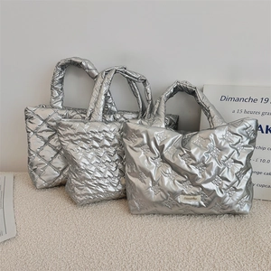 Close-up of silver quilted puffy handbags in diamond and heart patterns on a minimalist stand