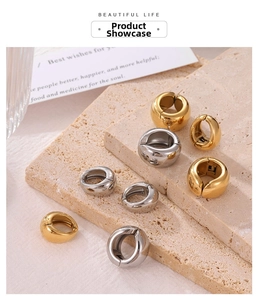 Close-up of chunky gold and silver hoop earrings on a beige natural stone background
