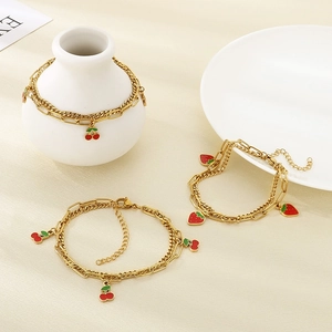 Detail of gold double-layer chain bracelet with cherry and strawberry enamel pendants