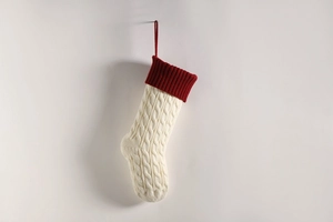 Detailed cable knit Christmas stocking in cream and red hanging on a white wall