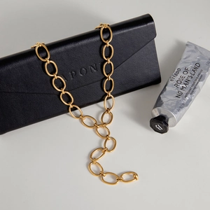 Detail of chunky gold chain necklace draped over a black envelope leather pouch