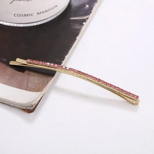 Detailed close-up of a long golden metal hair clip featuring sparkling pink rhinestones