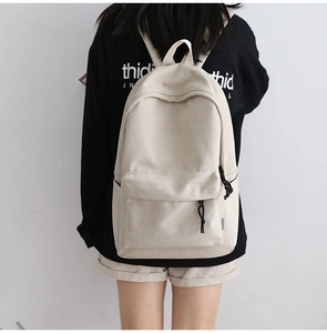 Back view of a person wearing a cream canvas backpack against a clean white wall