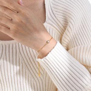 Minimalist gold chain bracelet with single round zircon worn on white knitted sleeve