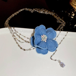 Détail d'une fleur en denim bleu et pendentif en cristal sur une chaîne en métal multicouche