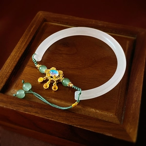 Détail d'un bracelet en jade blanc de style chinois avec fil vert et fermoir doré