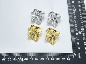 Detailed view of gold and silver textured wave earrings next to a measuring ruler