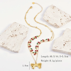 Detailed view of layered gold cherry necklace with bow pendant on a textured stone