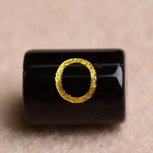 Macro shot of a black cylindrical bead with a textured gold circular pattern for DIY jewelry